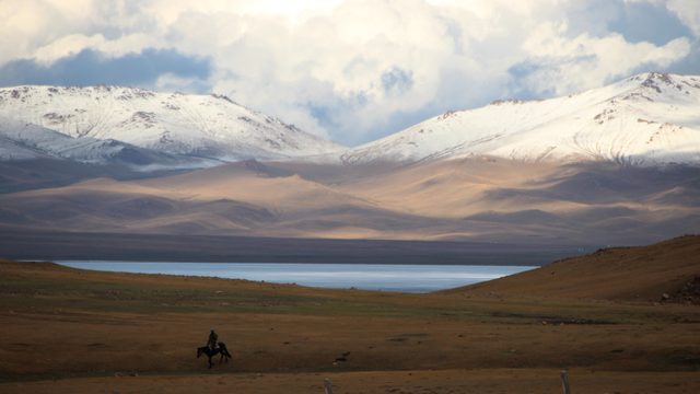 Ruiter te paard op de steppe bij het Song-Kulmeer, met besneeuwde bergtoppen onder een wolkenlucht