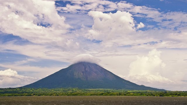De kegelvormige Concepción-vulkaan op het eiland Ometepe, met een wolkenkapje op de top, gezien over het Nicaraguameer